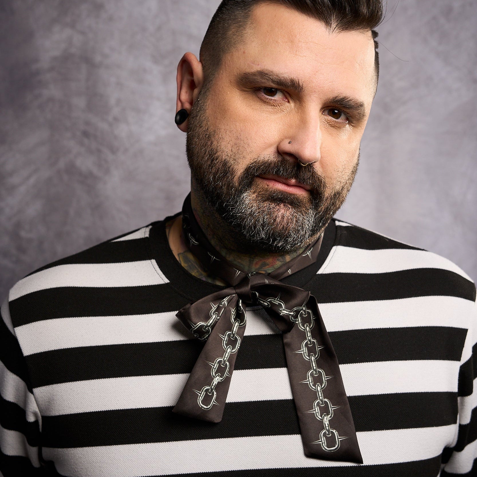 Man wearing a black and white striped shirt with a neckerchief against a gray background