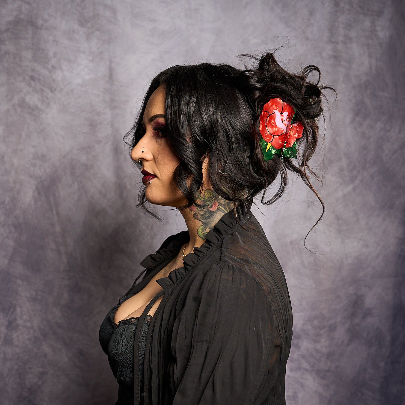 Woman with tattoos and a flower in her hair against a gray background